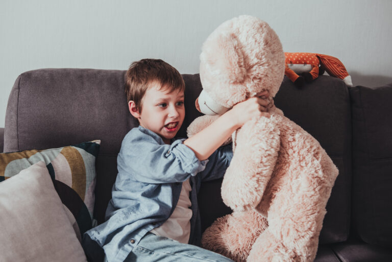 Child aggression. Irritated little boy suffocating a teddy bear at home. Bad relationship in family