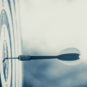 Close up red dart arrow hitting target center dartboard on sunset background. Business targeting and